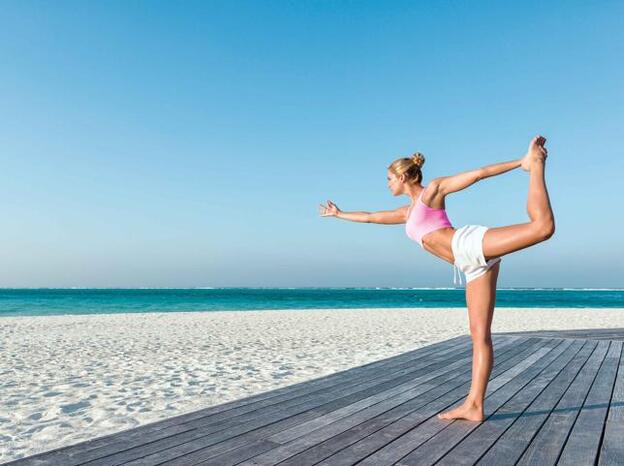 Una mujer practicando yoga en la playa./getty