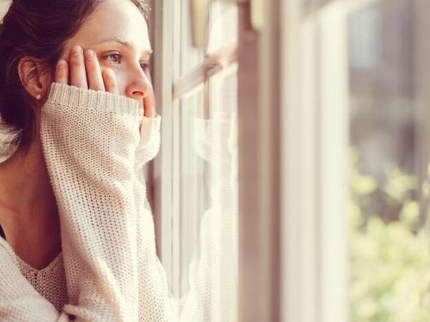 Una mujer pensativa mirando por una ventana./getty