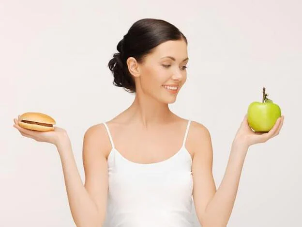 Una mujer, con una hamburguesa en una mano y una manzana en la otra./gtres