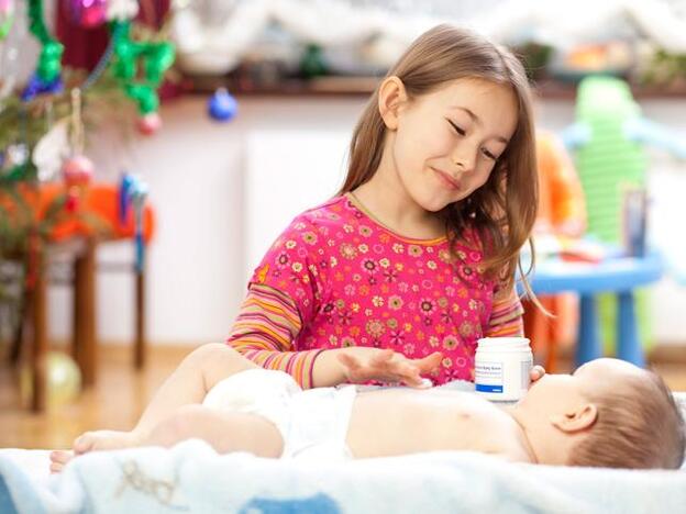 Una niña dando crema a un bebe./gtres