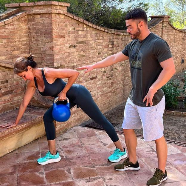 Elsa Anka realizando ejercicios de fuerza con una kettlebell ayudada por su entrenador personal. 