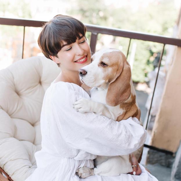 Mujer con el pelo corto sonriendo junto a su perro. 