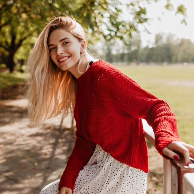 Mujer de pelo largo y rubio sonriendo en un parque. 