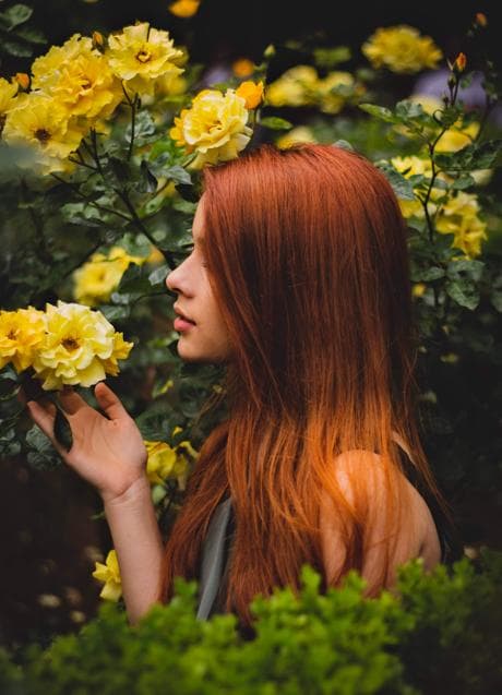 Red-haired woman smelling a yellow flower.  / Photo by Dg fotografo, in Pexels.