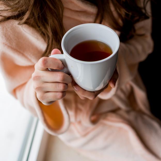 Mujer sosteniendo una taza de infusión de cardamomo. 