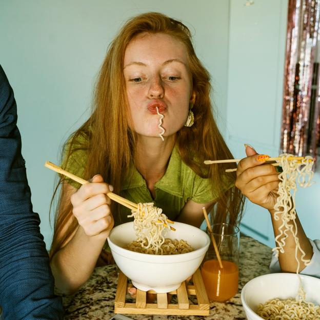 Mujer joven comiendo unos fideos con palillos chinos. 