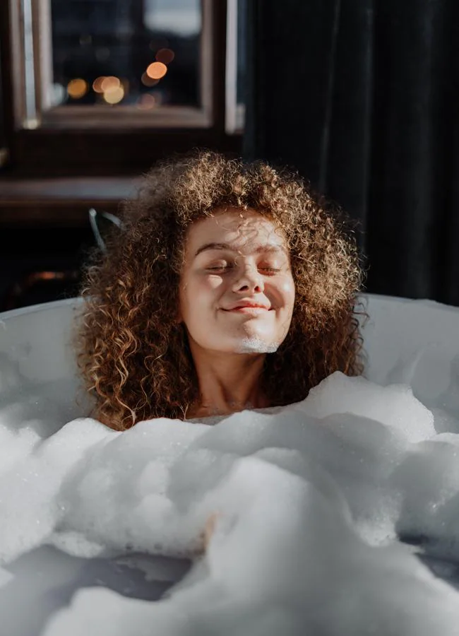 Mujer sonriente dándose un baño de espuma/PEXELS