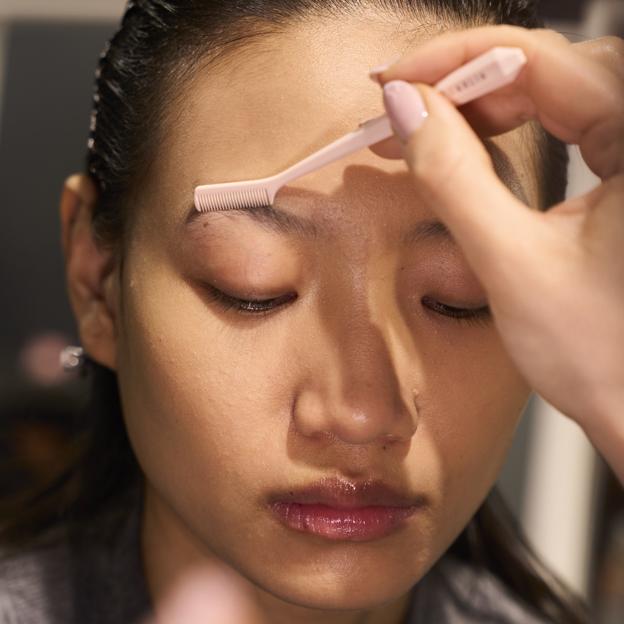 Una maquilladora peinando las cejas de una modelo.