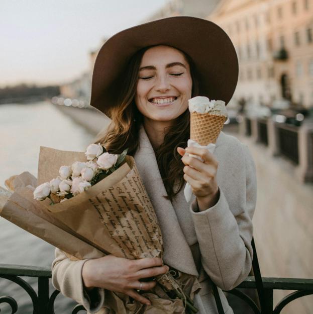 Mujer feliz tomando helado y sosteniendo flores. 