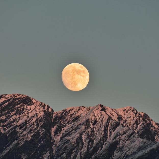 Una luna llena sobre montañas nevadas. 